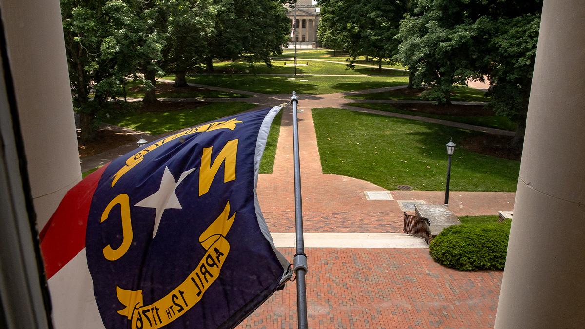 North Carolina state flag flying from South Building with view of Polk Place in the background on the campus of UNC-Chapel Hill.