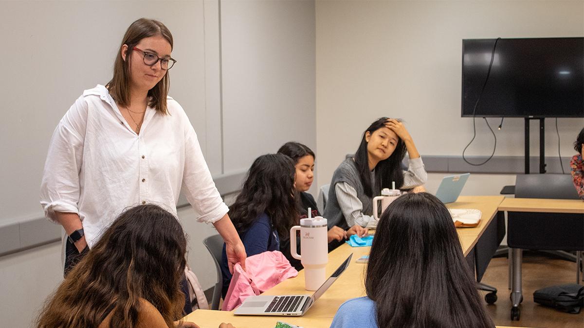 Woman wearing white top standing in front of students in conference room.